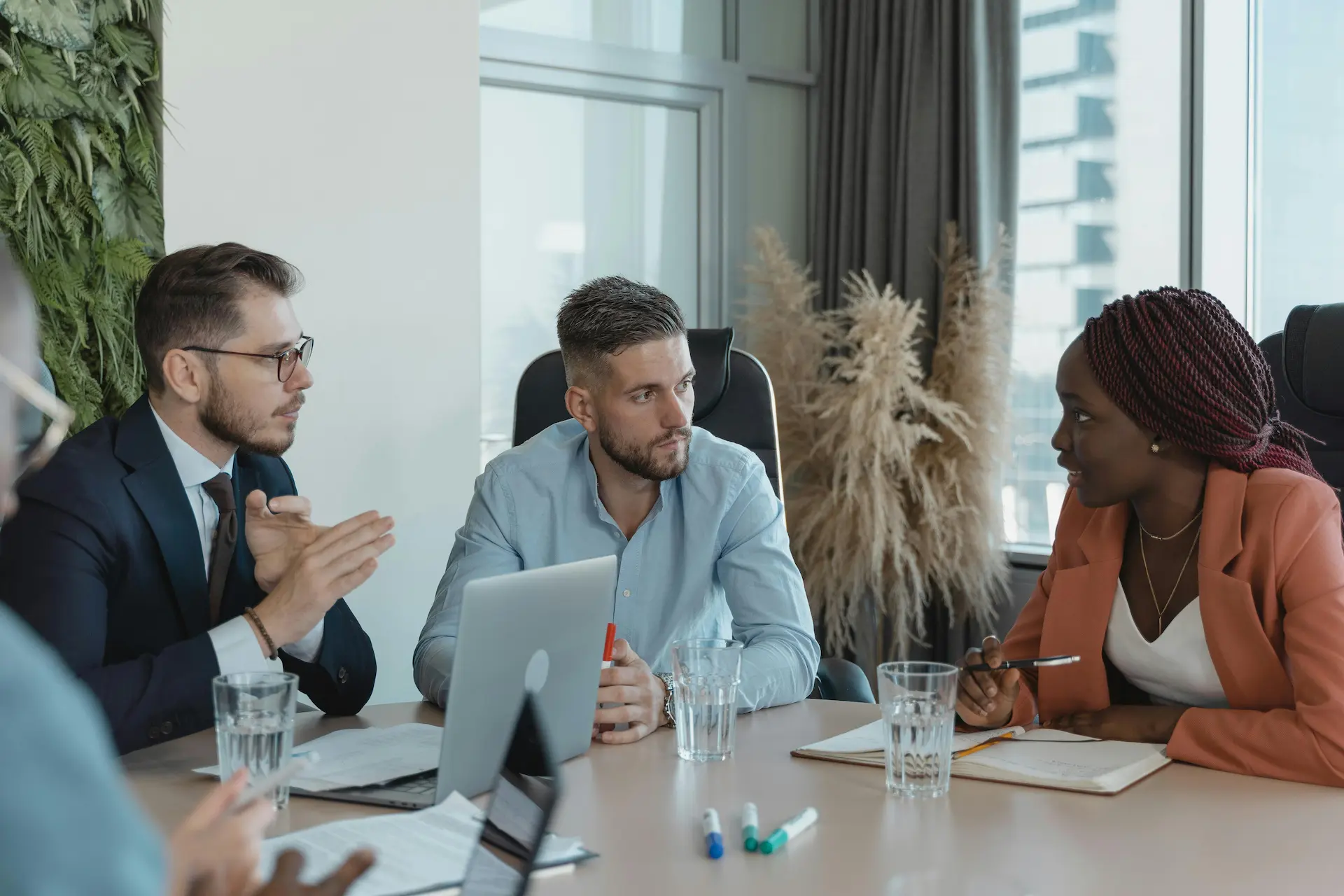 Four professionals in discussion at a conference table with a laptop